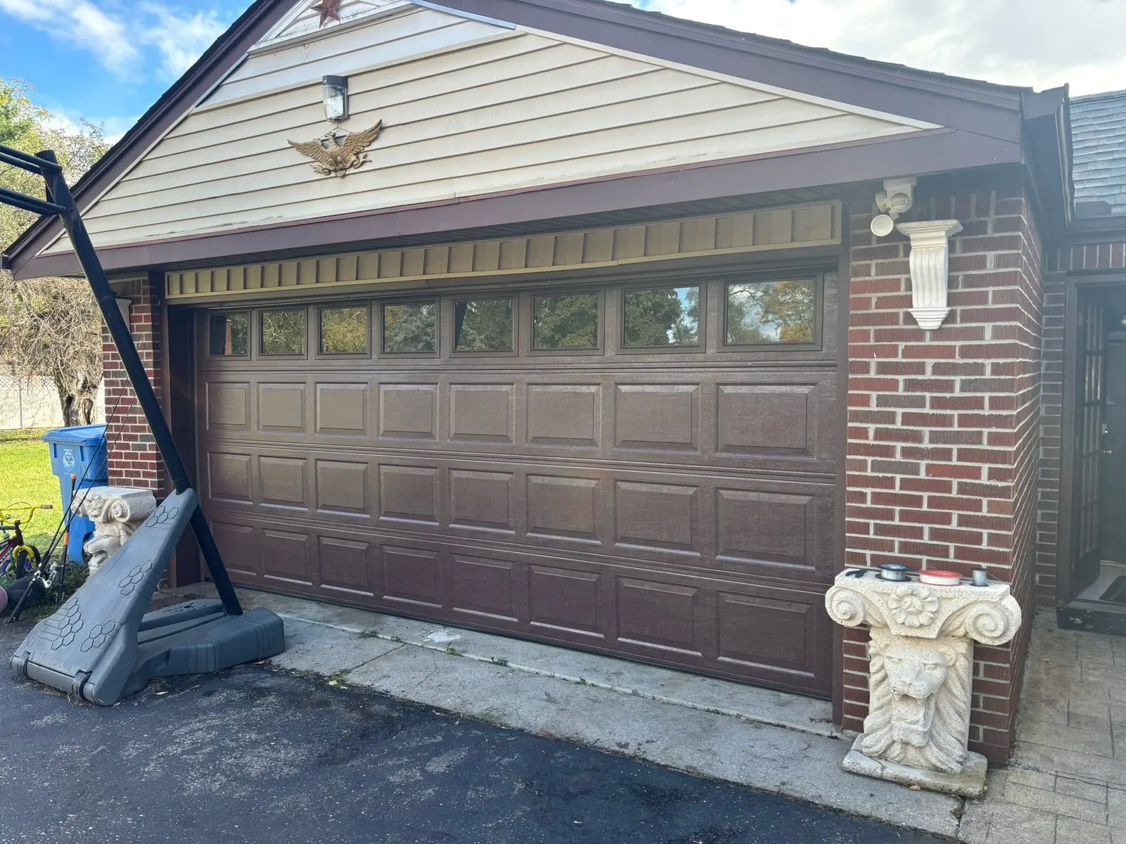 Brown raised-panel double garage door with a row of windows across the top section